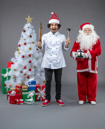 节日圣诞老人和男厨师在灰色墙上围着圣诞礼物的正视图圣诞老人帽子男性