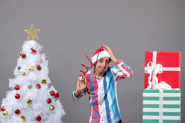 圣诞树前视图年轻人拿着他的螺旋弹簧圣诞帽靠近白色圣诞树年轻帽子春天