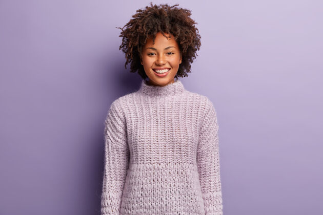 脆快乐的非洲裔美国女人的肖像 卷发 健康的皮肤 穿着紫色针织毛衣 在室内摆姿势 嘲笑有趣的东西单色人和积极卷发微笑非洲
