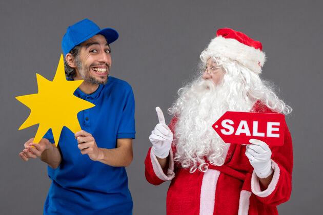 举行圣诞老人的正面图 男性信使手持销售横幅 灰色墙上有黄色标志庆祝快乐圣诞老人