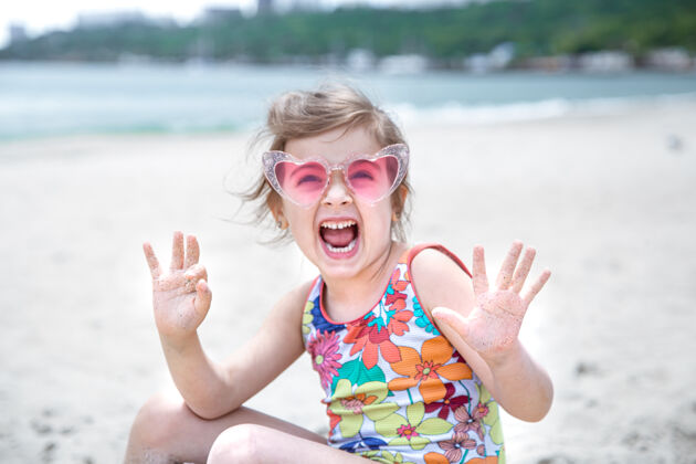 坐着一个戴眼镜的可爱小女孩正在海边的沙滩上玩沙滩童年孩子