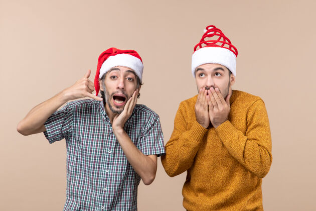 两个圣诞老人前视图两个圣诞节的家伙非常惊讶地戴着圣诞帽在米色孤立的背景前面男人惊喜