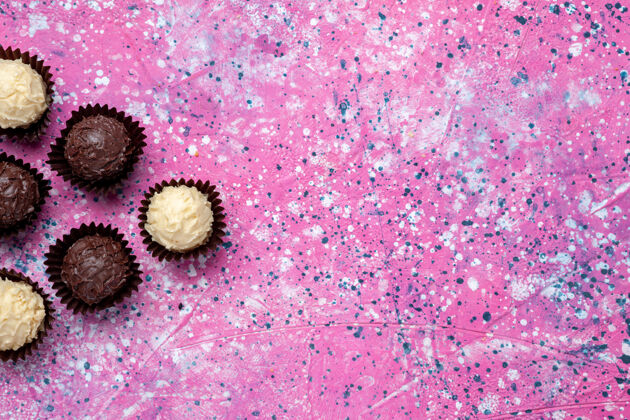 巧克力在粉红色的桌子上俯瞰美味的巧克力糖果白色和黑巧克力粉红糖果邦邦