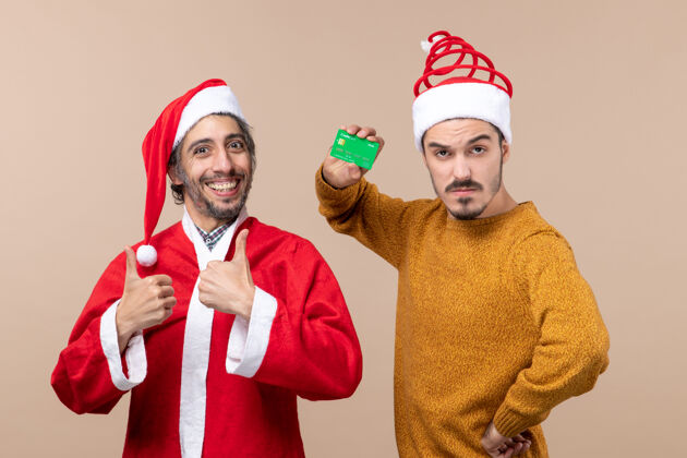 手正面图两个快乐的家伙 一个穿着圣诞老人的外套 另一个手放在米色孤立背景的腰部两个外套米色