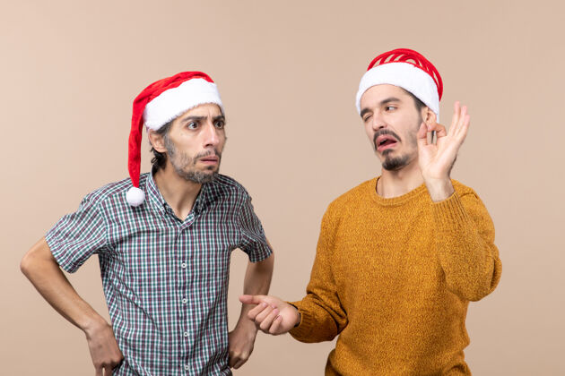 两个前视图两个戴圣诞帽的家伙一个在米色隔离背景上做“OK”标志男前面圣诞老人