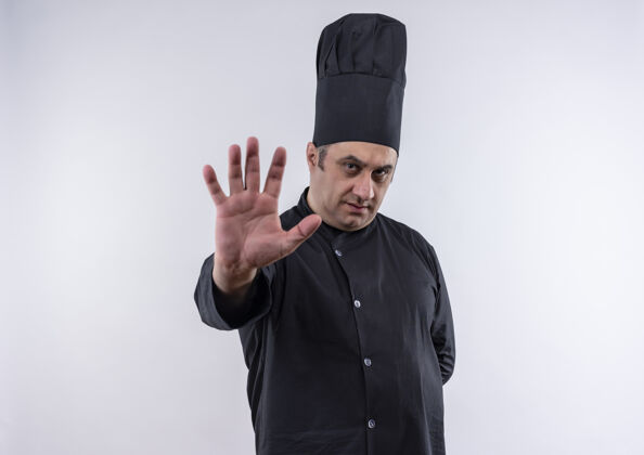 站住身着厨师制服的中年男厨师在隔离的白色墙壁上显示停止手势表情制服中年