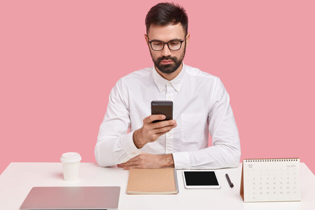 工作成功的大胡子老板穿着正式的白衬衫 拿着手机 拨电话号码 在浏览器里搜索信息 完美主义者个人行政人员智能手机