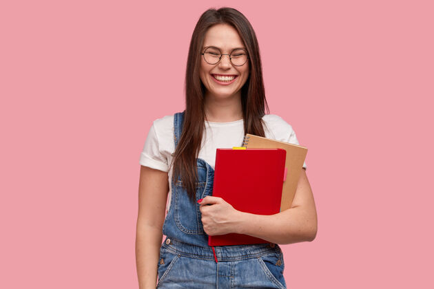 学术快乐微笑的少女 带着喜悦的表情 拿着两本教科书 咧嘴笑 笑得好计划学习工装裤