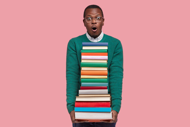 阅读情绪激动的惊讶黑人表情惊恐 拿着一堆教科书 害怕有许多任务要准备 粉红色背景上的模型高中沮丧恐惧