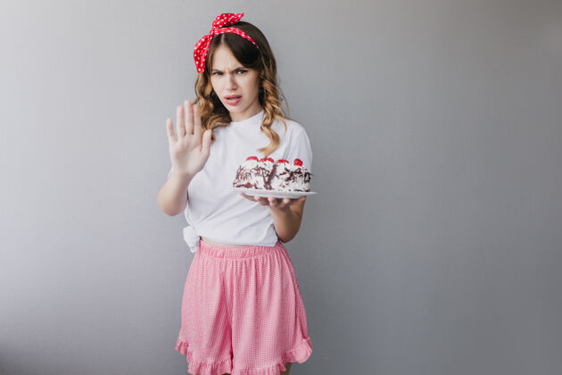 模特心烦意乱的穿着粉色裙子的女人拿着生日蛋糕摆姿势时尚的女孩拿着一个孤立的馅饼快乐水果美味