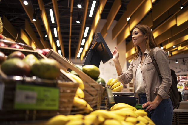 水果超市里的女人用自助数字秤测量水果的重量购物狂微笑商品
