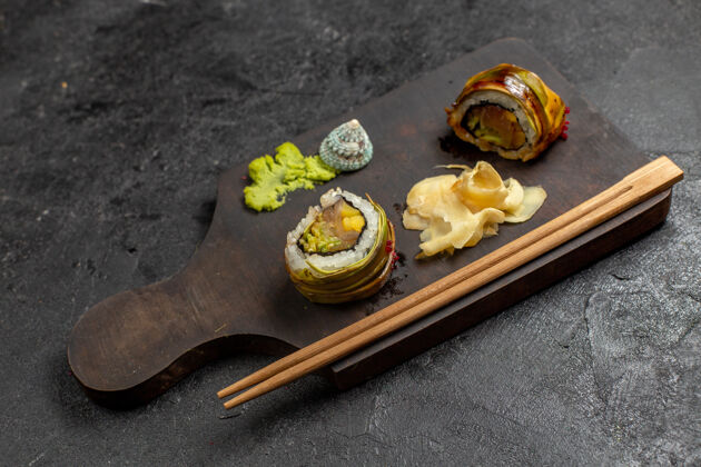卷美味的寿司餐前视图-绿色的马萨比鱼片卷和灰色墙壁上的棍子日本前面米饭