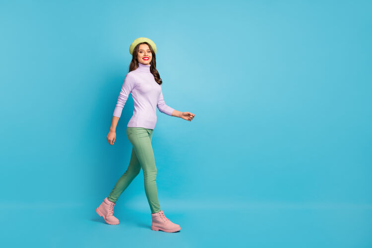 欢乐美丽的旅游女士走在街上的全长资料照片国外游客穿绿色贝雷帽紫色高领套头衫长裤靴子孤立的蓝色墙壁漂亮女孩运动