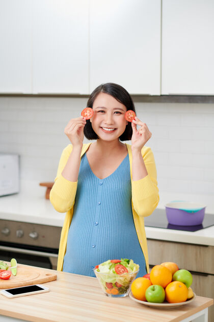 女性孕妇抱着西红柿片捂着眼睛 怀孕期间健康饮食和营养的概念烹饪亚洲食物