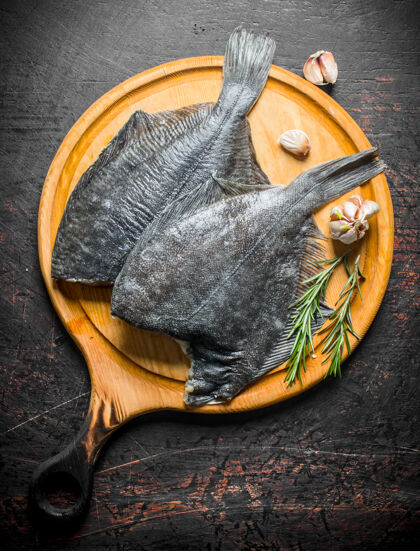 海鲜生鱼比目鱼放在木质砧板上 黑色乡村餐桌上放着大蒜和迷迭香鱼蛋白质膳食