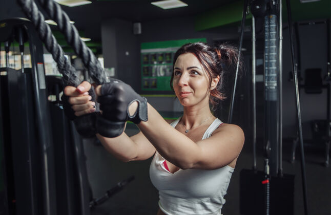 缆索机年轻苗条的女人在健身房练习用绳索伸展手臂努力决心健康