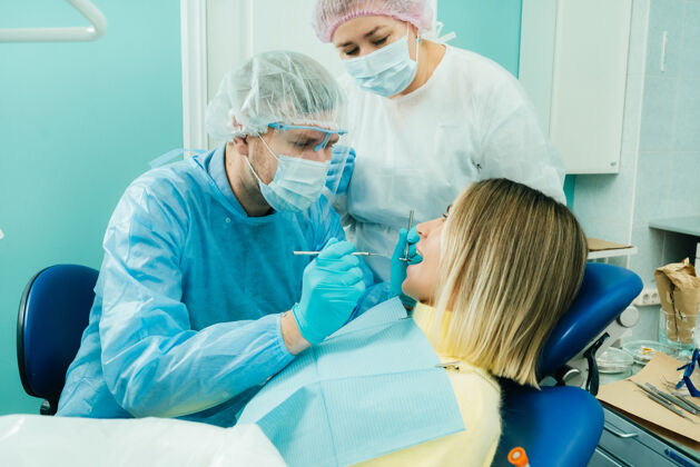 妇女一个戴着防护面具的牙医坐在他旁边 和一个助手在牙科诊所治疗病人卫生牙齿正畸医生