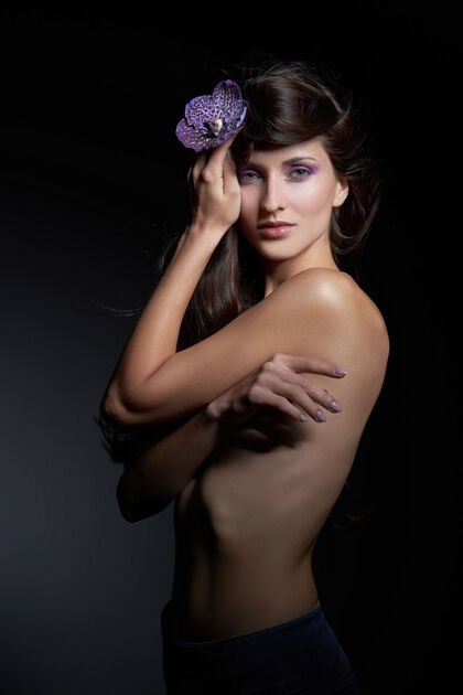 女性一个裸体女人的美丽肖像 手里拿着一朵紫色的花 挂在黑暗的墙上天然化妆品 天然化妆品年轻化妆品皮肤