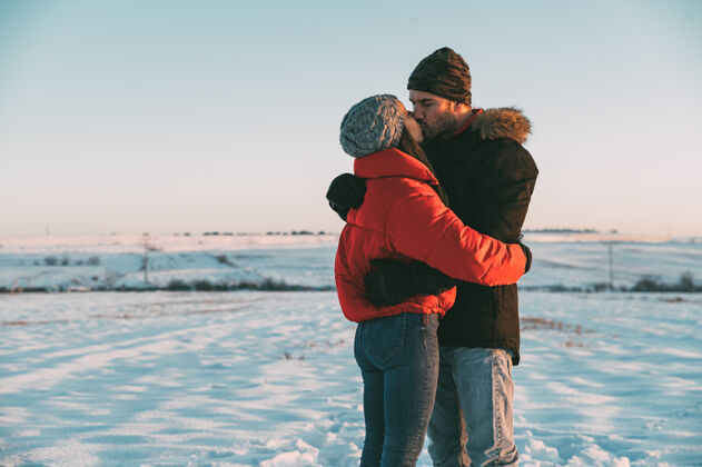 寒冷一对热恋中的情侣穿着暖和的衣服 在雪域冬日的乡间拥抱亲吻享受拥抱日落