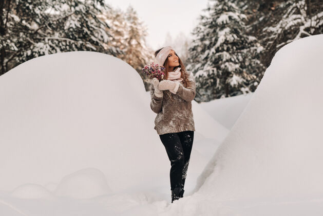雪冬天 一个穿着毛衣 手里拿着一束花的女孩站在大雪堆中间天春天霜冻