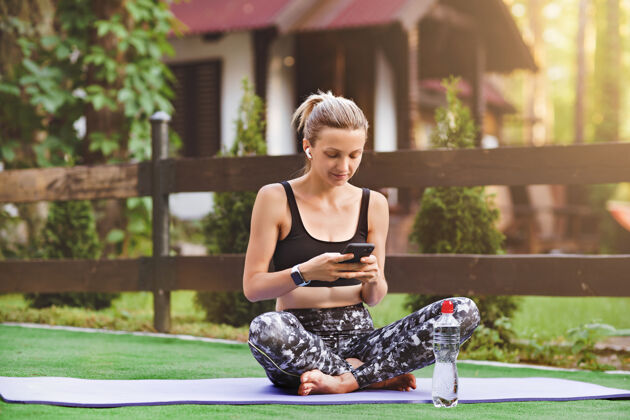 减肥精力充沛的女运动员坐在紫色的垫子上用手机在健康的体育博客上发表体育评论电话私人教练放松
