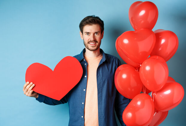 男朋友情人节和爱情概念带着浪漫礼物 心形气球和情人明信片 站在蓝色背景上微笑着等待情人的年轻人男人微笑日子