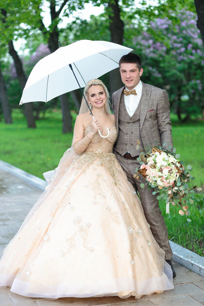 夫妇快乐的新郎新娘打着白色雨伞 在夏天的公园里露天婚礼毕业庆祝学生