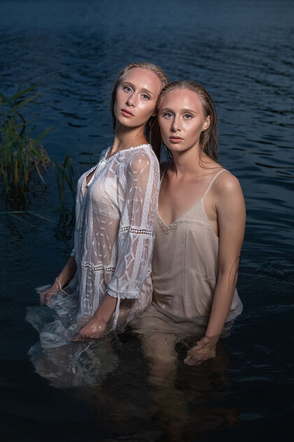 女士夏日夜晚 两个金色长发的孪生妹妹在湖水里摆出一身轻装优雅性感水