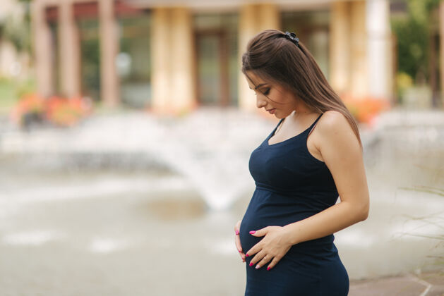 外面美丽的年轻开朗的孕妇站在喷泉的背景下微笑人阳光