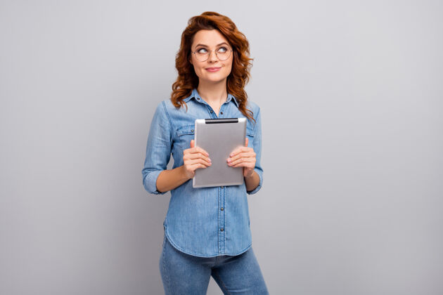 自由职业者有兴趣的女人的肖像拿着使用平板电脑思考想法看文字空间决定社交媒体应用后穿现代服装隔离灰色墙壁休闲女人牛仔裤