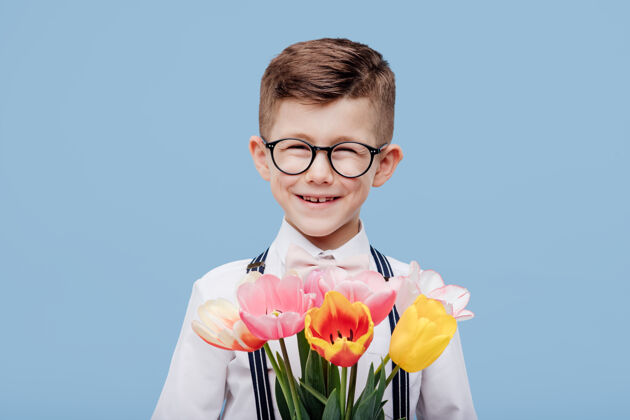 惊喜戴着眼镜的微笑的小男孩手里拿着花 隔离在蓝色的墙上童年小看