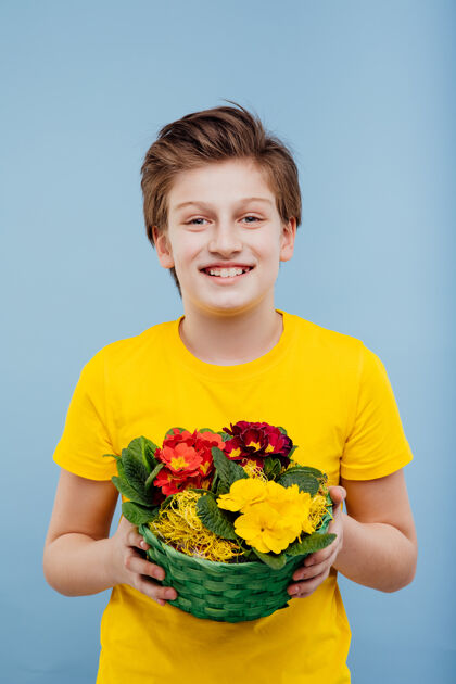 肖像快乐的男孩手里拿着花篮 穿着黄色的t恤 隔离在蓝色的墙上 复制空间孩子五颜六色花