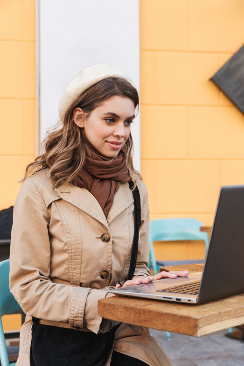 短信一个快乐的年轻漂亮的女人坐在咖啡馆里用笔记本电脑走在户外户外街道户外