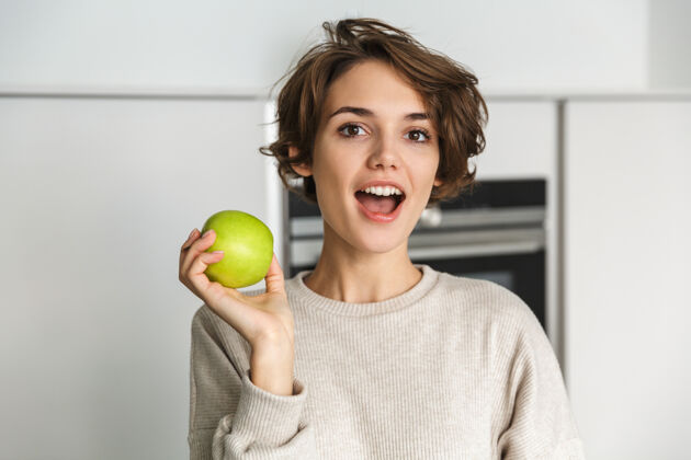 肖像微笑的年轻女子在厨房里拿着青苹果漂亮品味新鲜