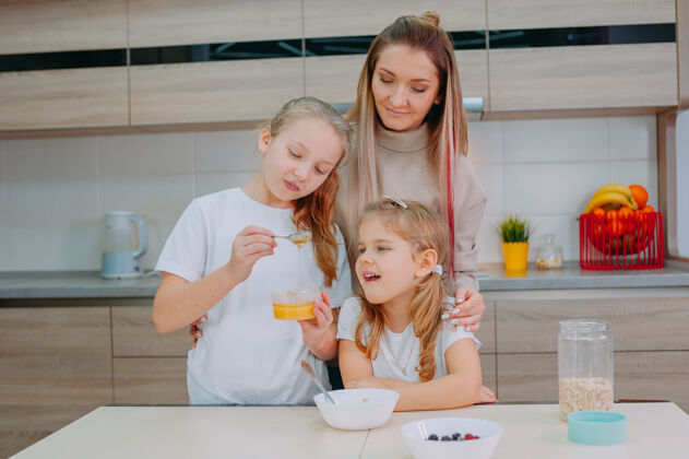 谷物一位母亲和她的两个女儿在厨房里给燕麦片加蜂蜜债券父母自然