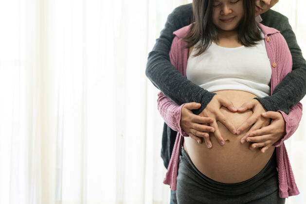 父母夫妻幸福怀孕年轻的孕妇在怀孕的肚子里抱着孩子期望怀孕床