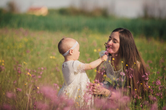 小年轻的妈妈和可爱的小女儿在野花地里散步和玩耍女儿罂粟花田野