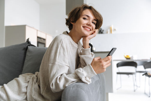 休闲快乐的年轻女子坐在家里的沙发上 用手机成人软件浏览