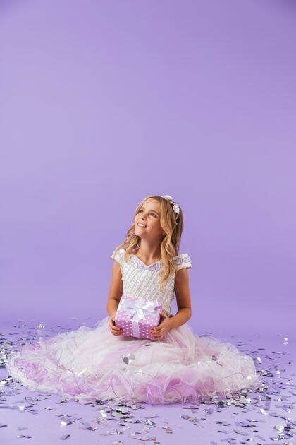 小穿着公主裙的漂亮小女孩孤零零地坐在紫罗兰色的墙上 手里拿着礼物盒年轻束女儿