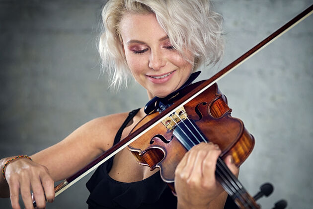 学生年轻漂亮的金发女人穿着黑色的裙子在白色的砖墙背景上拉小提琴音乐艺术家小提琴