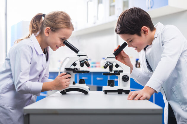 室内年轻的科学家不错快乐聪明的孩子们站在对面 看着显微镜 一边上生物课集中实验室样品