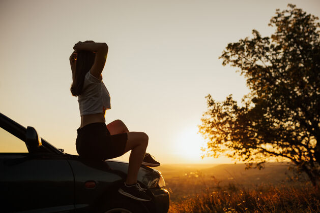 户外坐在路边汽车上的年轻女子日落她欣赏美丽的风景和日落乐趣魅力华丽