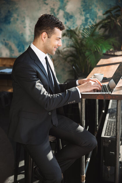 网络帅气的年轻商人穿着正装在咖啡馆里使用笔记本电脑的照片成年人户外工作