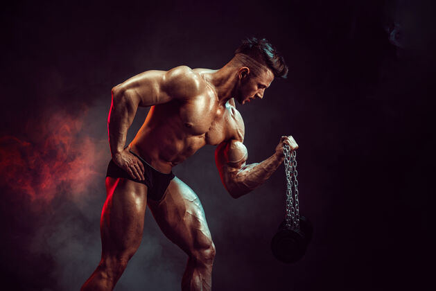 锻炼运动员在工作室里用烟在黑暗的墙上锻炼肌肉强壮的健美运动员拥有完美的腹肌身体完美男子