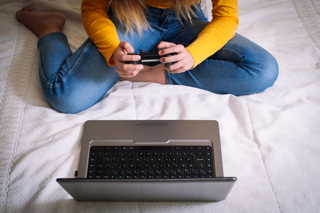 微笑坐在床上玩电脑游戏的年轻女子看快乐游戏