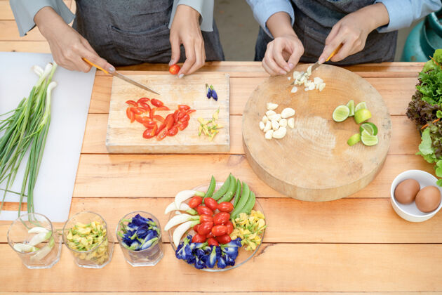 自制两位亚洲女性用刀在木板上切大蒜和西红柿 在那里放半青柠 豇豆 蝴蝶豆 葱 豌豆和鸡蛋 然后准备午餐洋葱颜色蔬菜