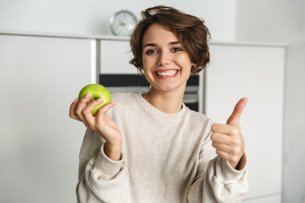 持有微笑的年轻女子在厨房里拿着青苹果苹果放松年轻