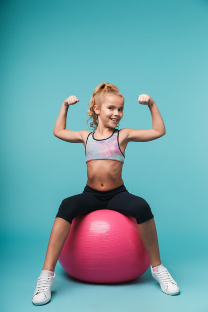狂喜快乐的小女孩穿着运动服和健身球隔着蓝色的墙做运动小体操童年