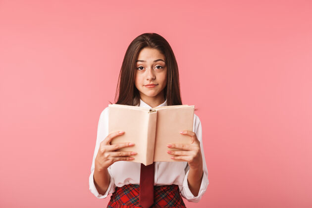 姿势可爱的女孩15-16岁的画像 穿着校服看书 孤立地站在红墙上青少年青少年请