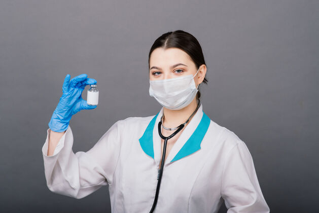 人严肃的女医生戴着医用口罩拿着注射器和疫苗隔离在灰色上面罩制服医疗保健